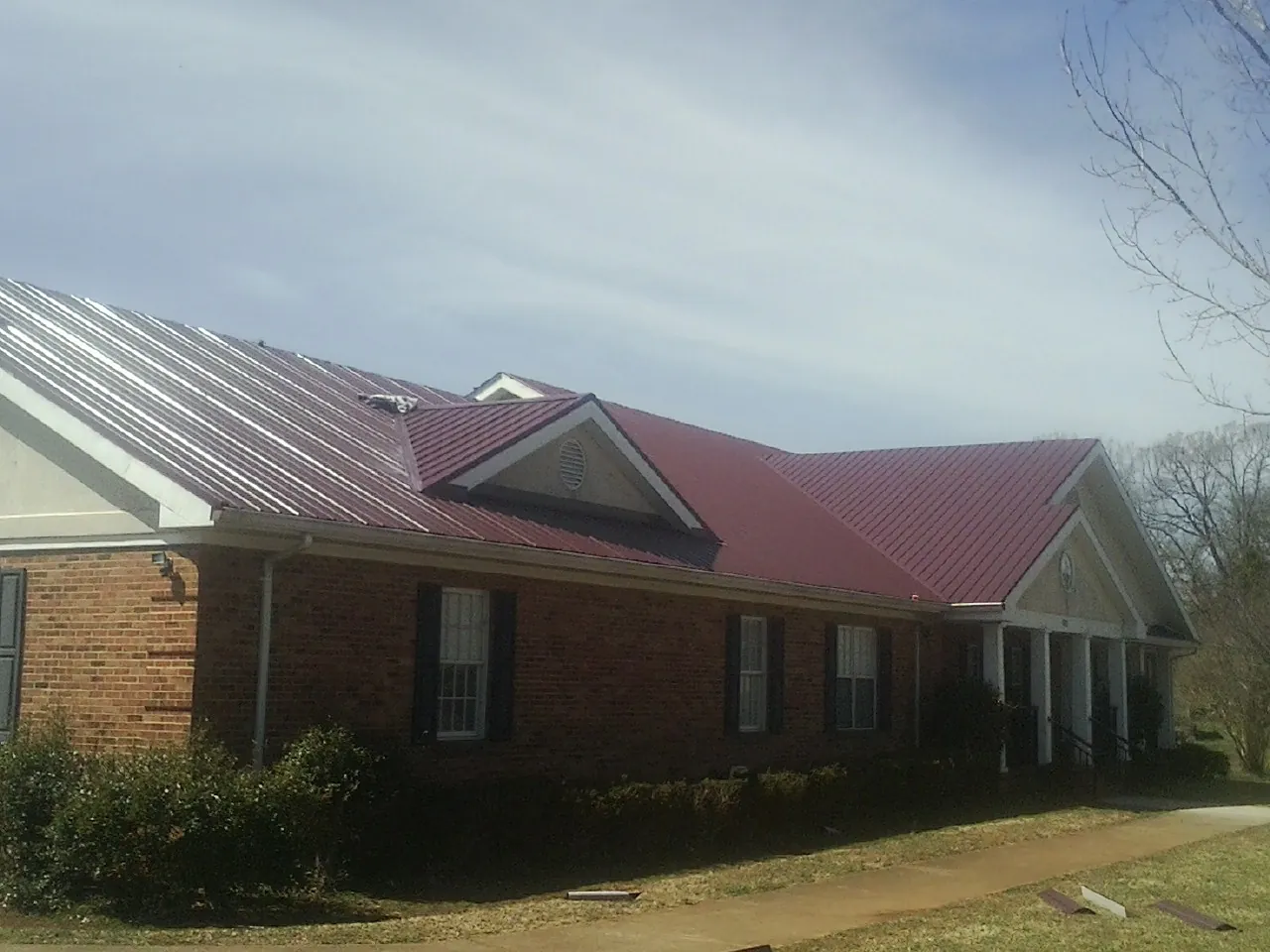Red metal roof with gabled entries on a long brick building, from a Hail Damage Roof Repair job in East Thetford