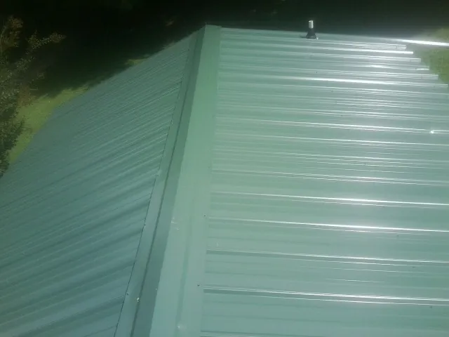 New green metal panels meeting at the ridge of a roof — Flat Roof Repair work by our crew in East Thetford