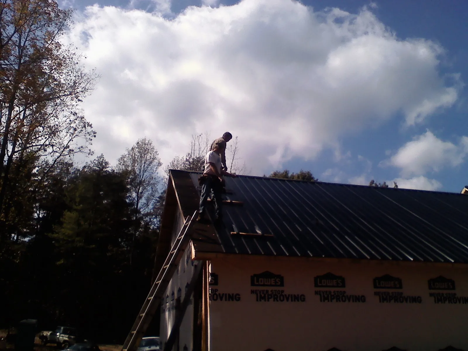 Roofer fastening dark metal panels high against a cloudy sky, from a Roof Inspection job in East Thetford