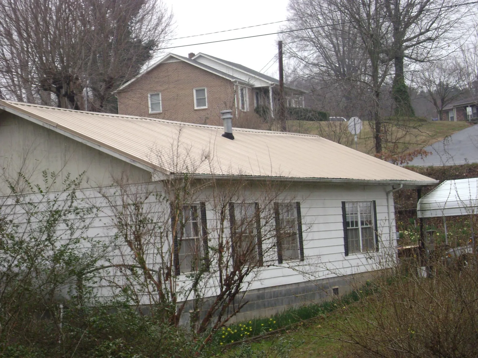 Tan metal roof on a white sided house set into a hillside — Commercial Roofing by Roofing Brothers in East Thetford